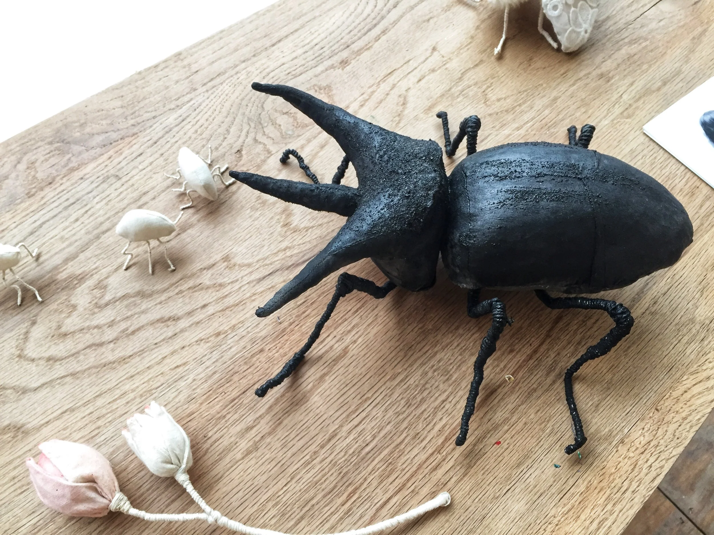 A black, artsy sculpture of a beetle on a wooden surface surrounded by small fabric mice.