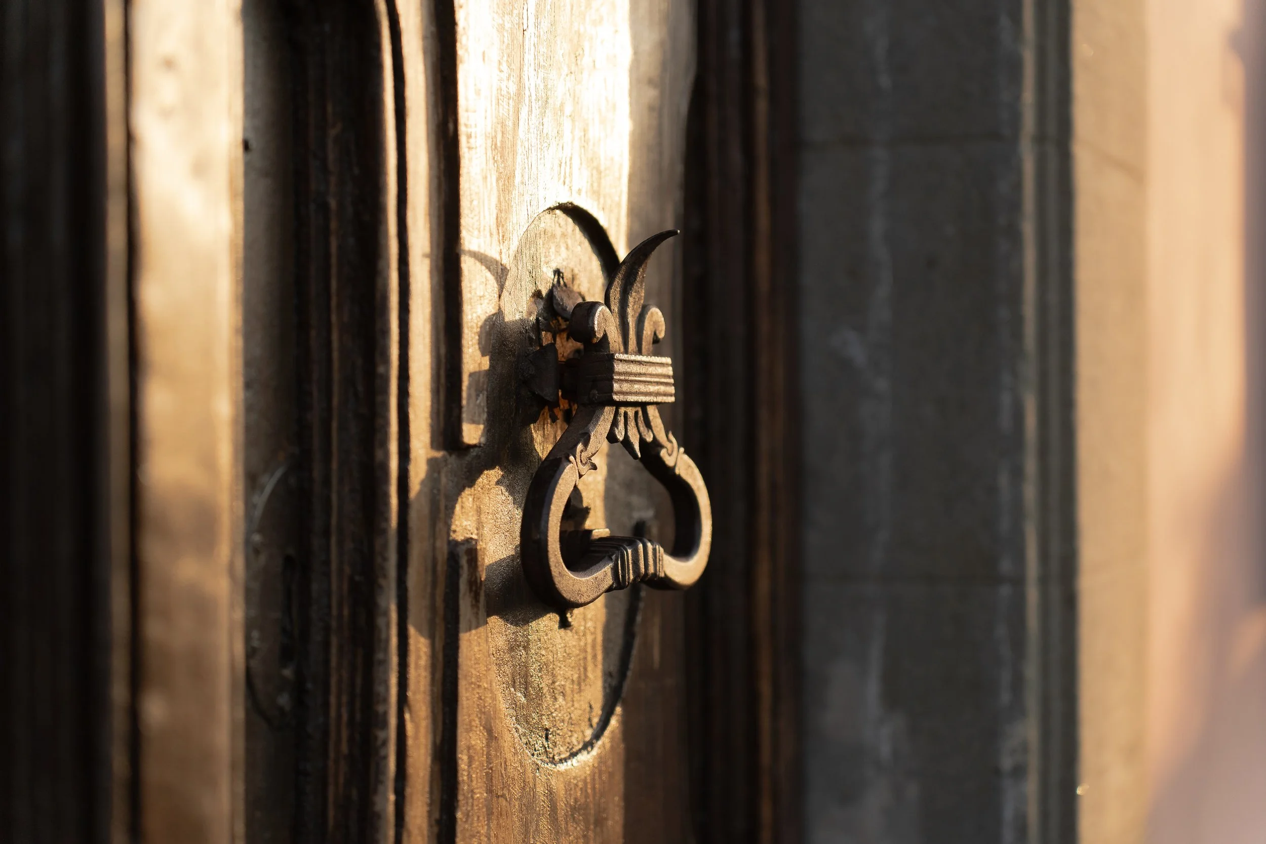 Close-up of an antique metal door knocker mounted on a wooden door, with sunlight casting shadows.