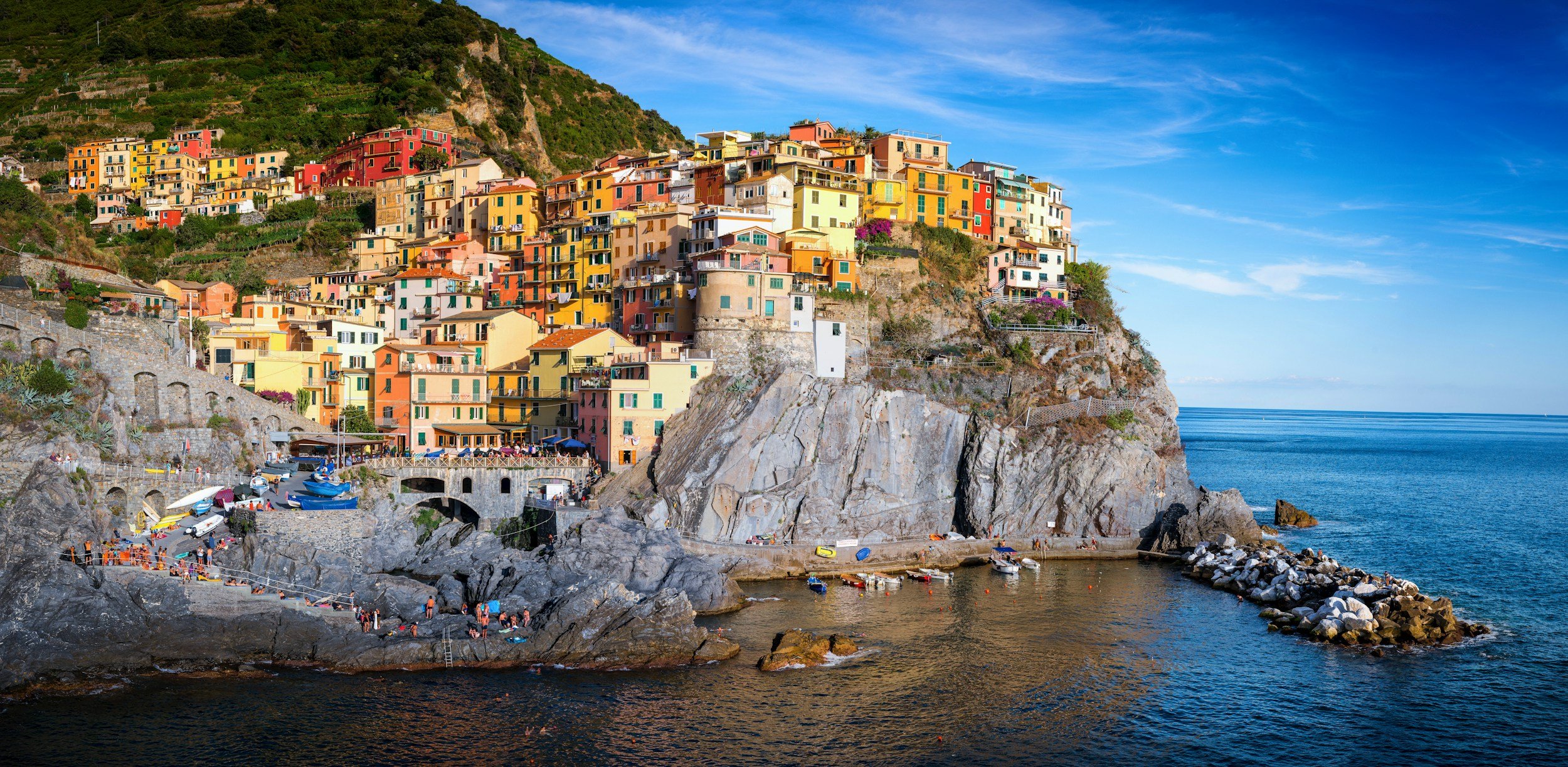 Colorful houses on a hillside overlooking the sea with a small harbor and boats at the bottom.