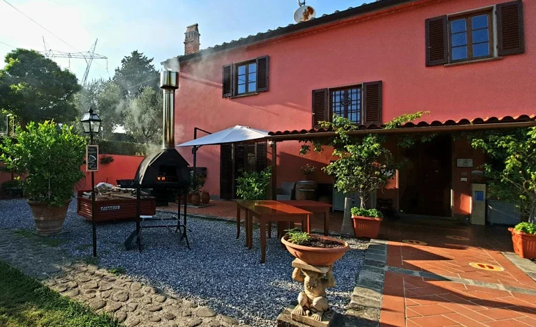 A pink house with open windows, outdoor barbecue grill, table, potted plants, and stone pathway in the backyard.