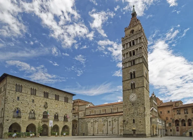 A historic stone tower with a clock, part of an old city square, under a partly cloudy blue sky.