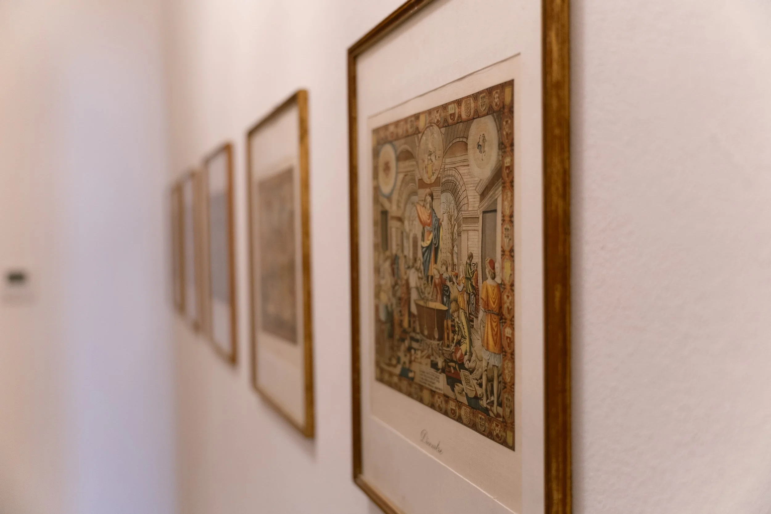 A series of framed artwork hung on a plain white wall in an art gallery or museum.