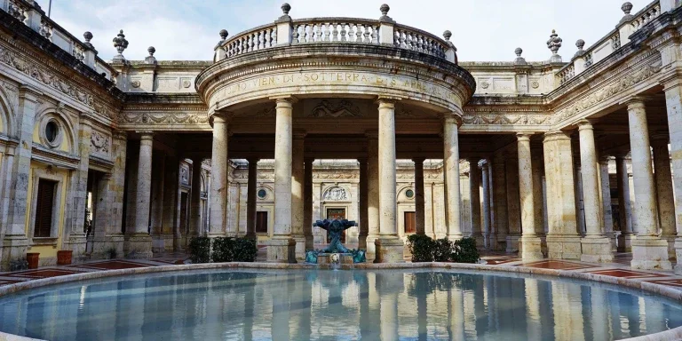Historic Italian-style building with columns, a fountain, and a circular balcony, featuring intricate architectural details.