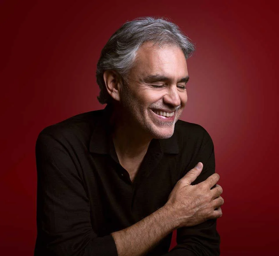 A middle-aged man with gray hair smiling, wearing a black shirt, against a red background.