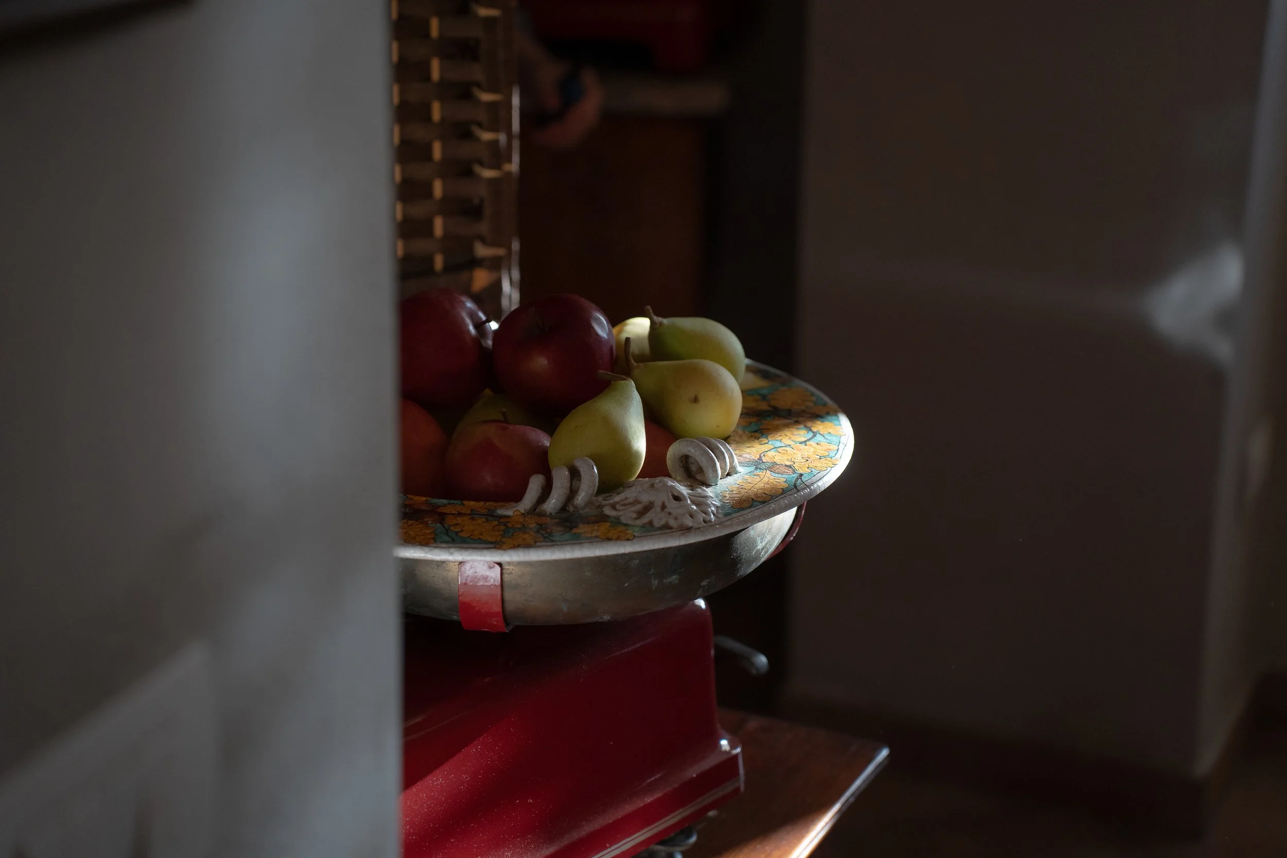 A bowl with apples and pears on a floral tablecloth in a dimly lit room.