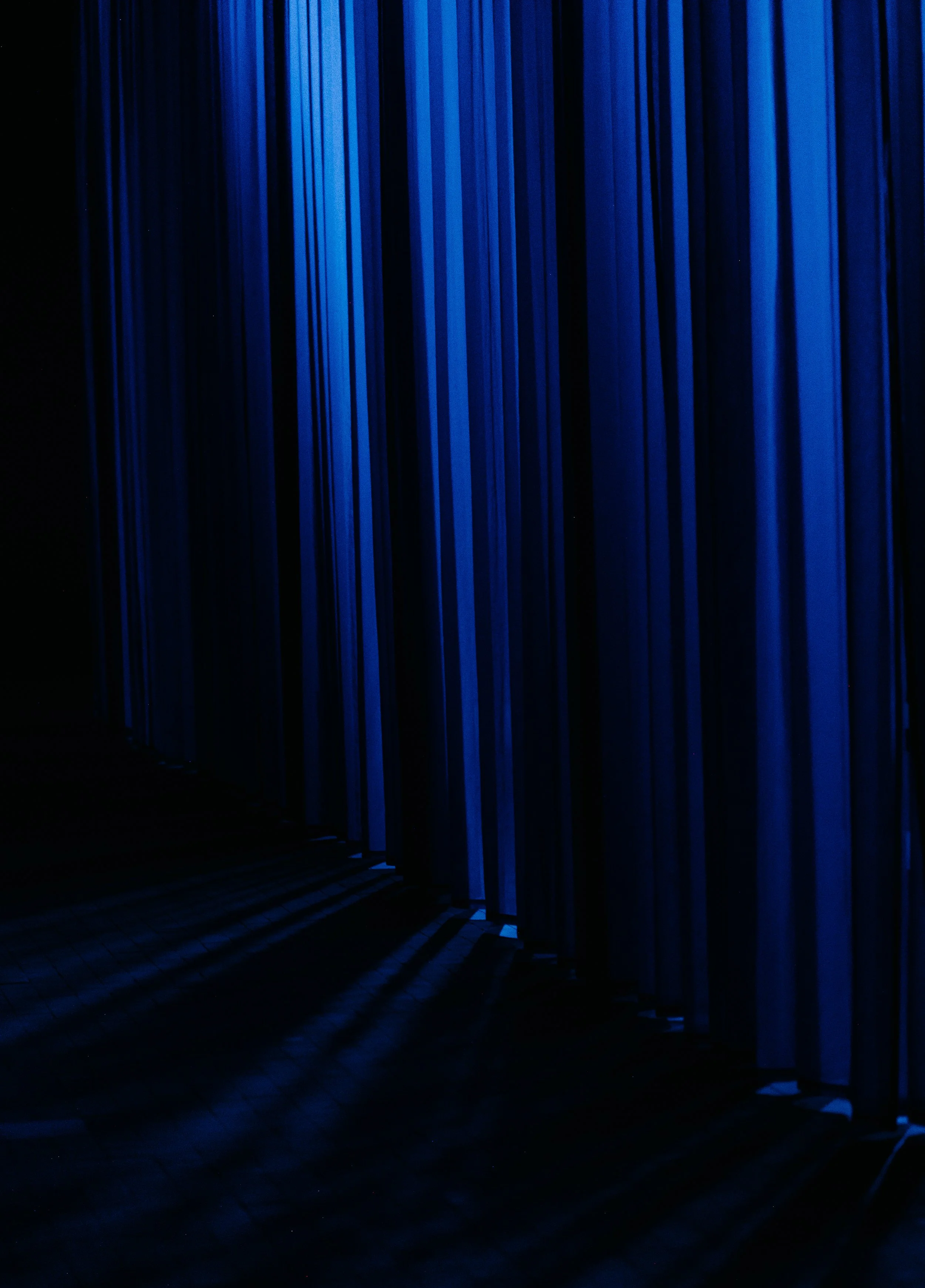 Dark room with blue curtains or panels and shadows cast by light.