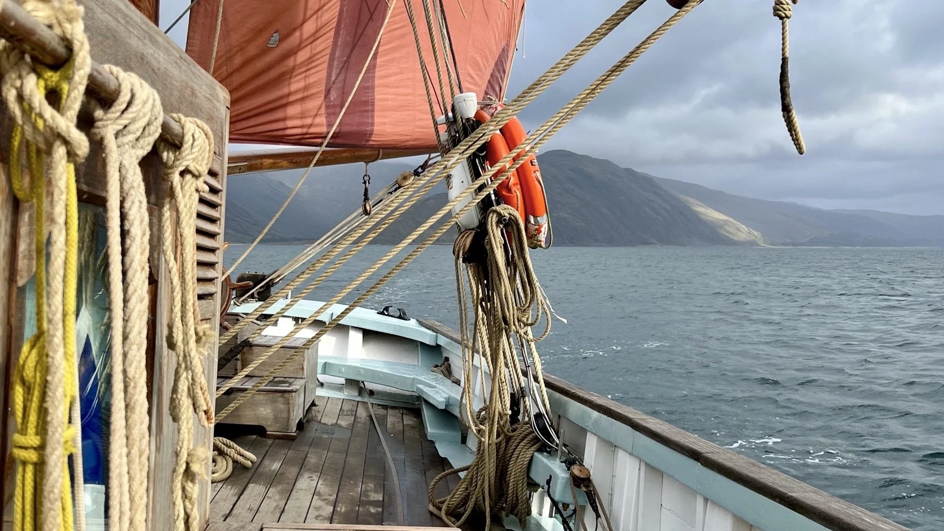 Ropes and equipment on a Provident with a sail, water, and hills in the background.