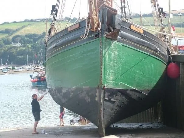 Provident is docked at a harbor, with two children and an adult nearby, and other boats and green hills in the background.