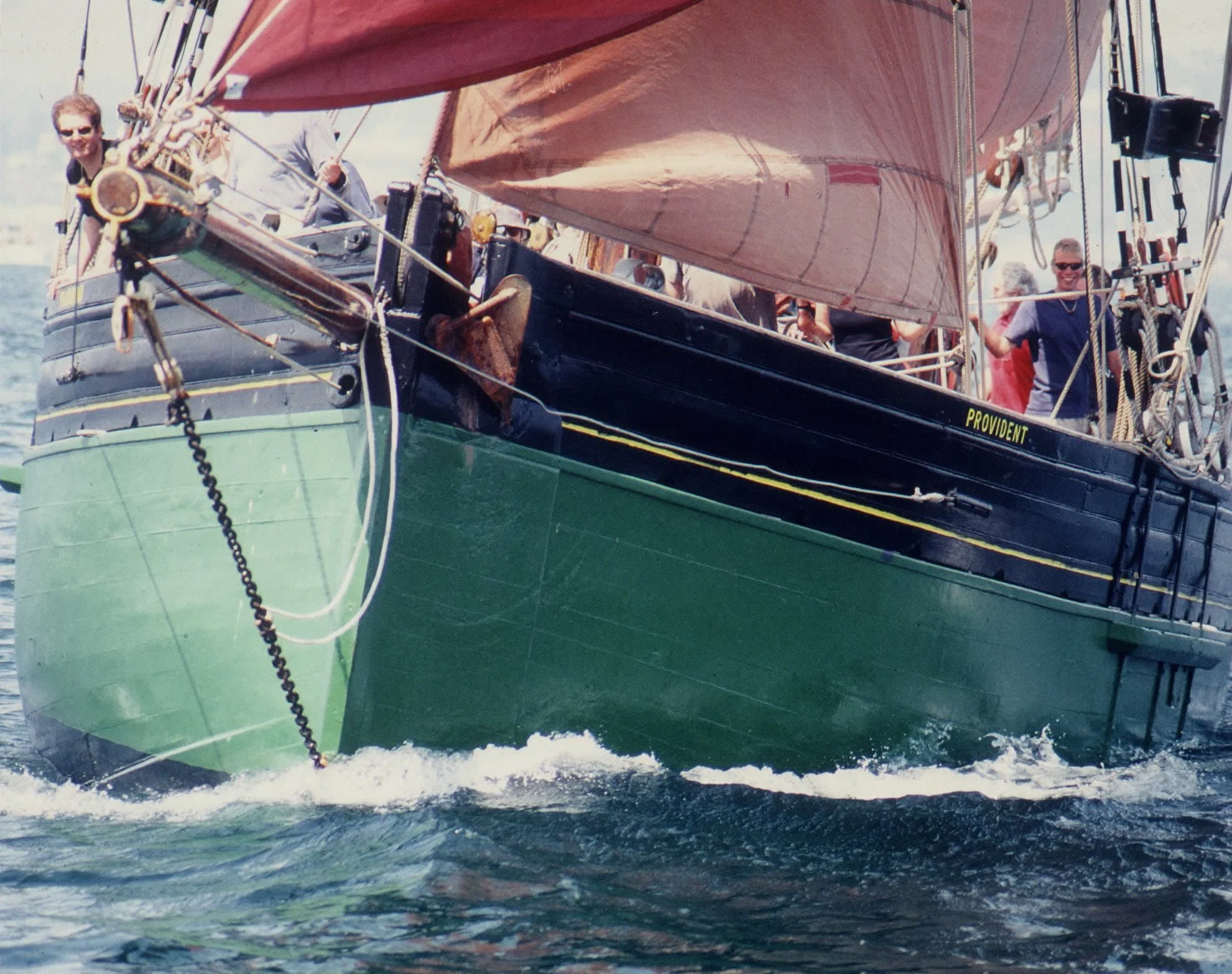 Provident with red sails on the water, with people onboard smiling and enjoying the sailing adventure.