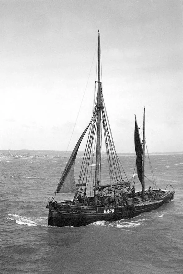 Black and white photo of Provident with two masts sailing on the water, with land visible in the background.