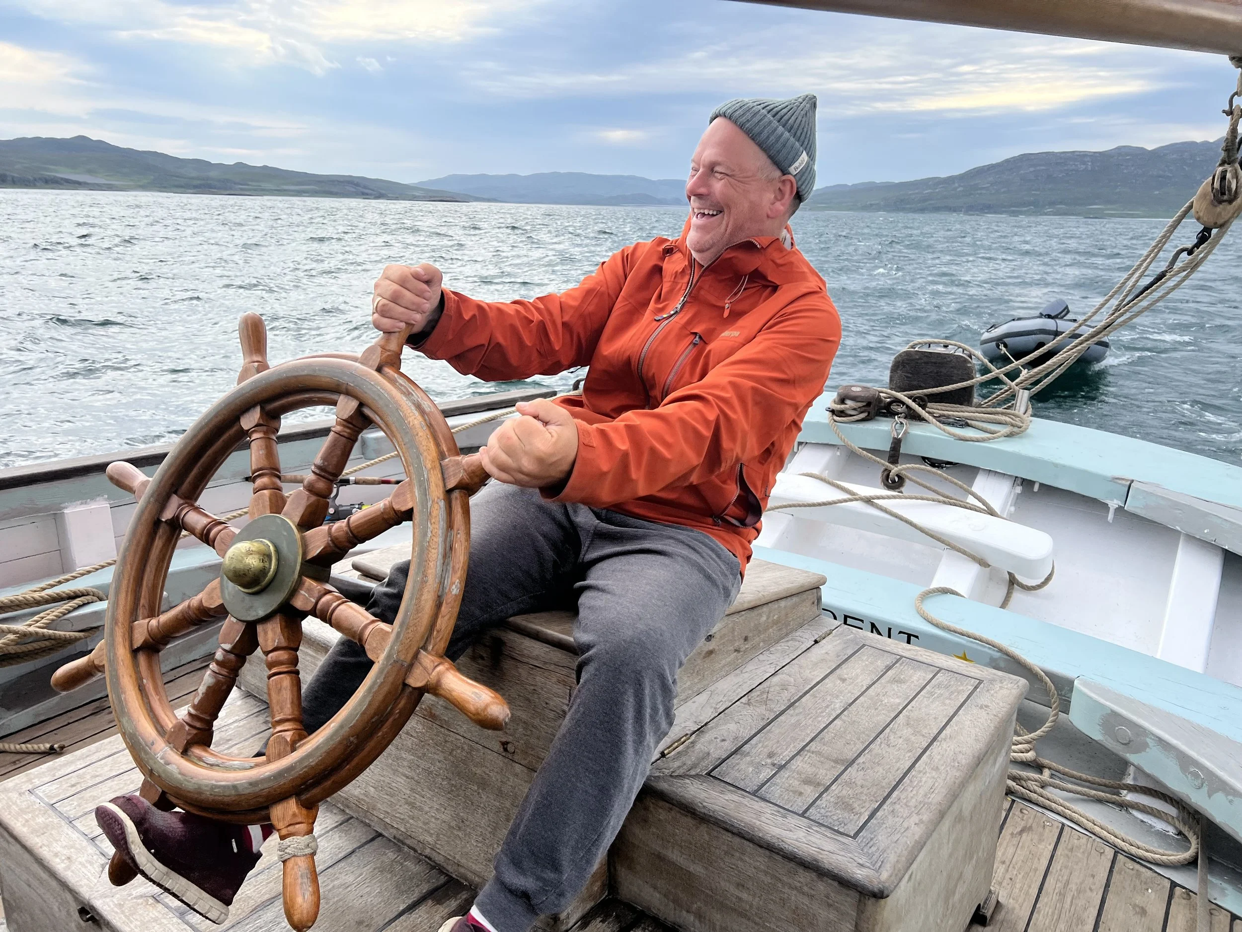 A cheerful man wearing an orange jacket and gray beanie steering Provident.