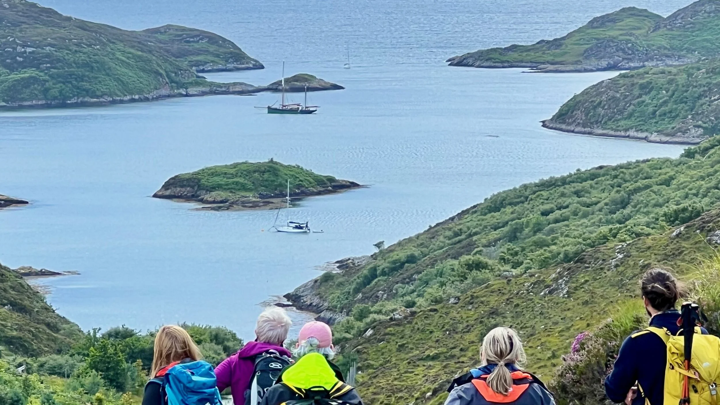 Group of hikers with backpacks overlooking a scenic coastal bay with islands and Provident, lush green hills on each side.