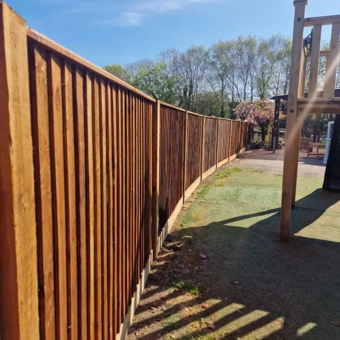 View of a newly installed wooden fence in a backyard, with trees and clear blue sky in the background.