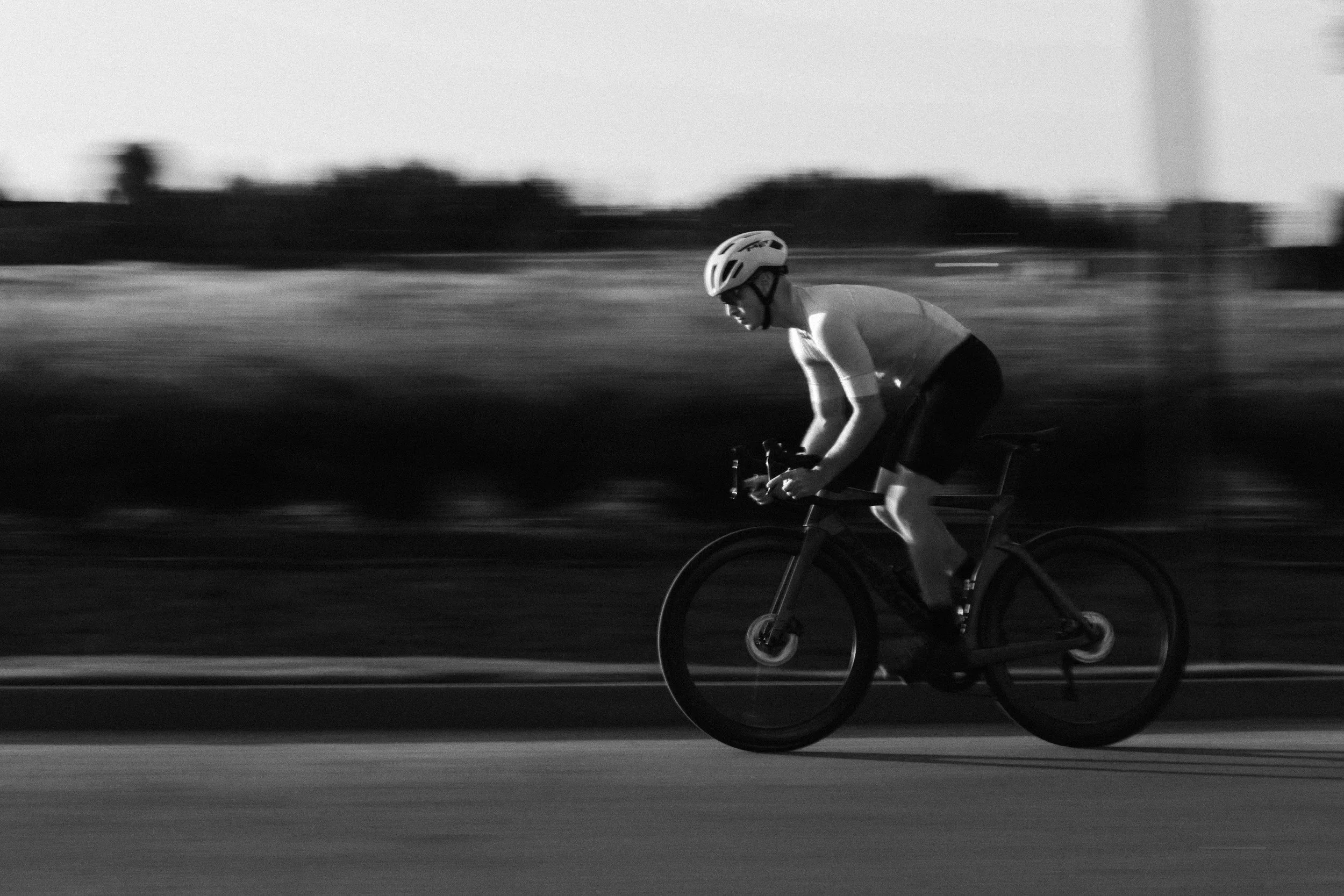 Ein Radfahrer trägt einen Helm und fährt auf einer Straße, die im Schwarz-Weiß-Bild dargestellt ist.