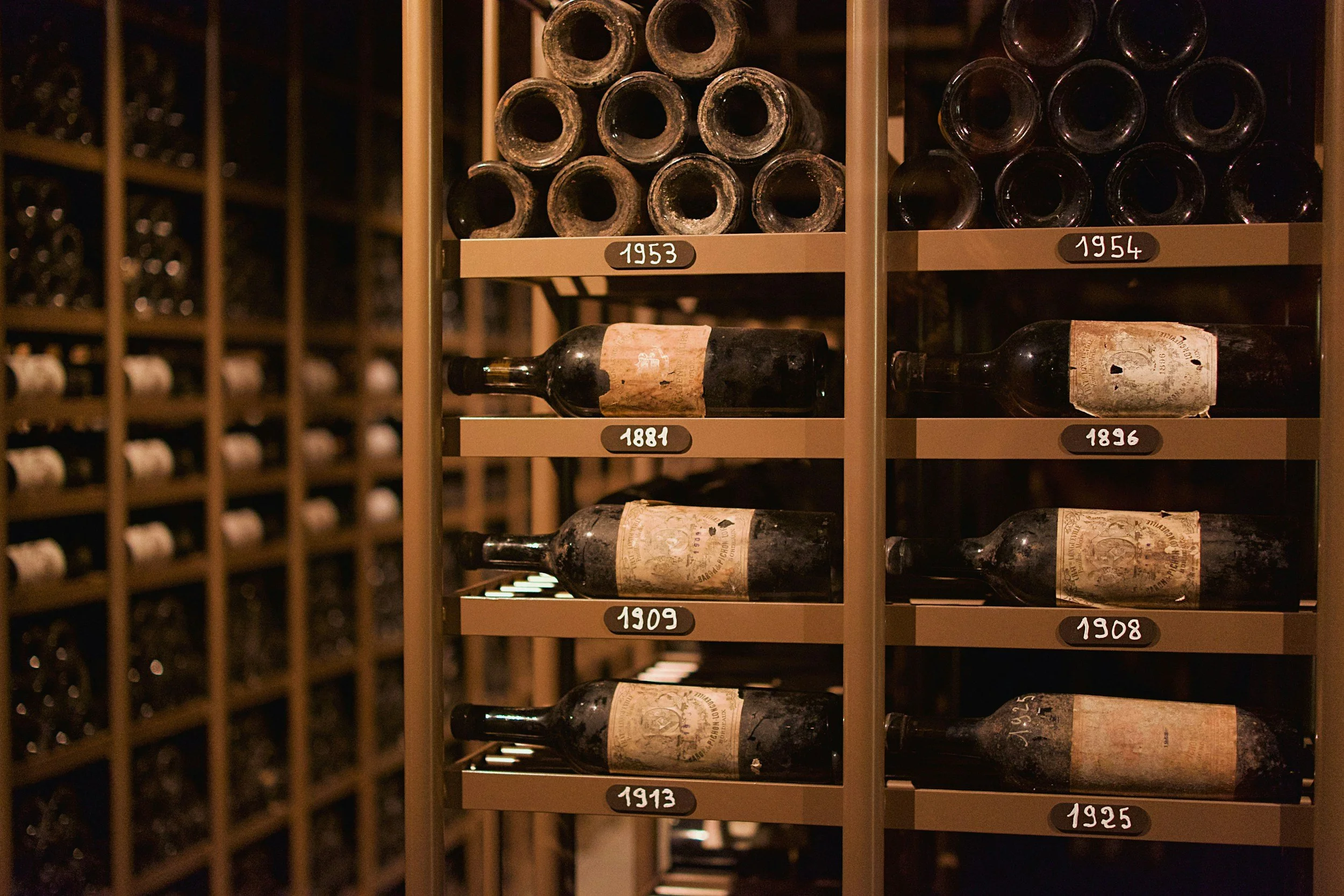 Vintage wine bottles stored on metal shelves with labels displaying years from 1881 to 1958.