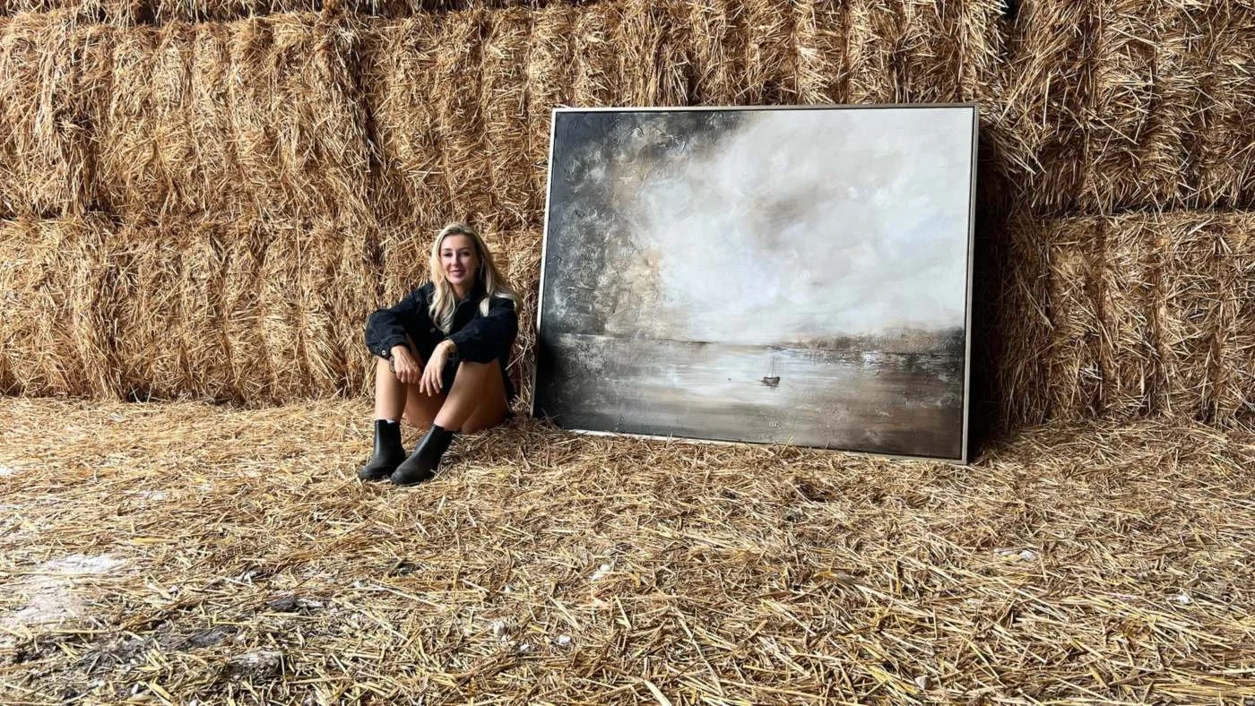 Joanna Green sitting on straw beside one of her large paintings