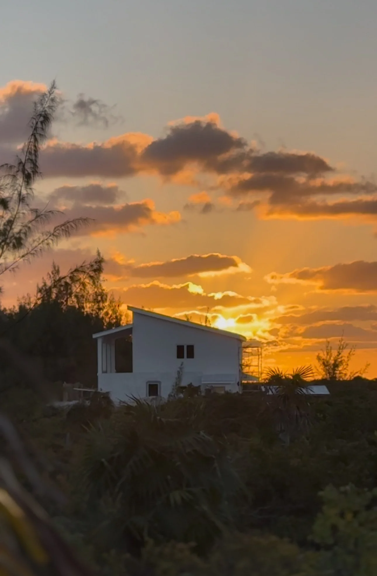 A modern white house on a hill during sunset with a sky filled with clouds.