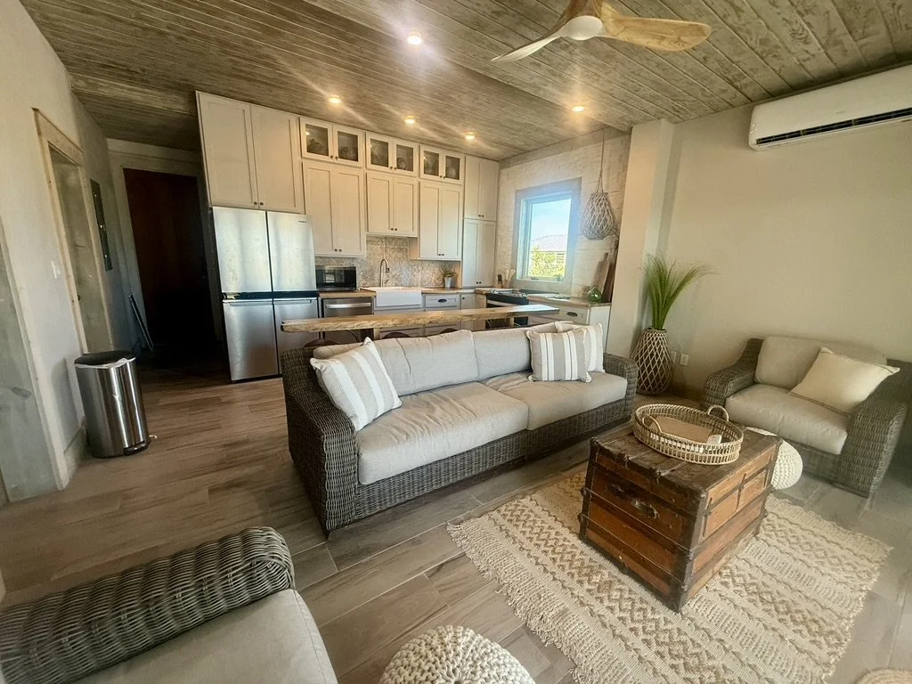Open-concept living room and kitchen with beige furniture, wooden ceiling, and modern appliances.