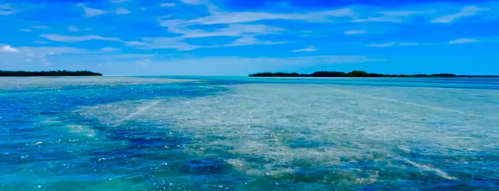 Sarcastic rainbow over an ocean with small islands in the distance and a partly cloudy sky.