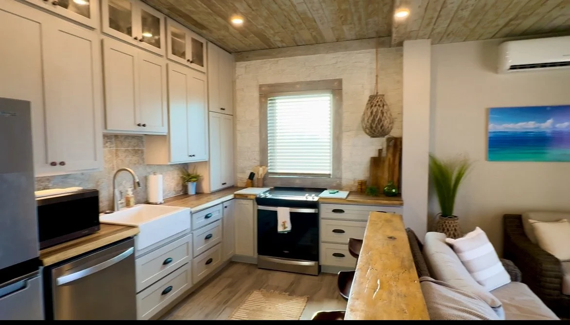 Kitchen with white cabinets, a black stove, a window with blinds, a microwave, a stainless steel refrigerator, and a bar counter with brown chairs.