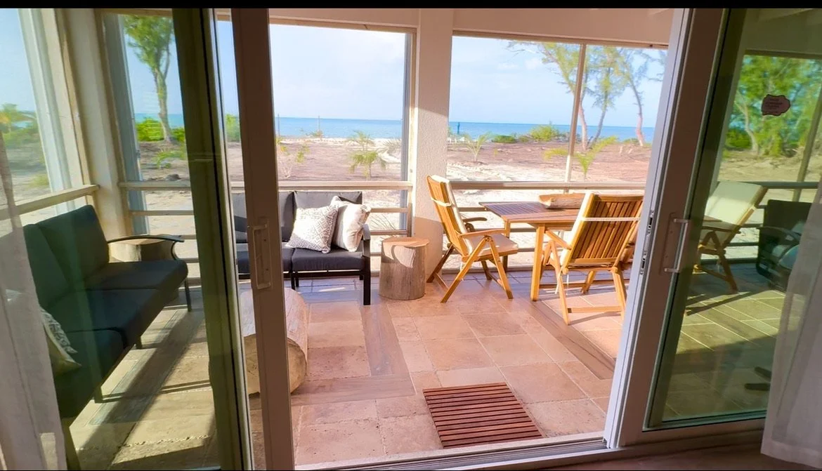Beach view from a screened porch with seating and a wooden dining table and chairs.