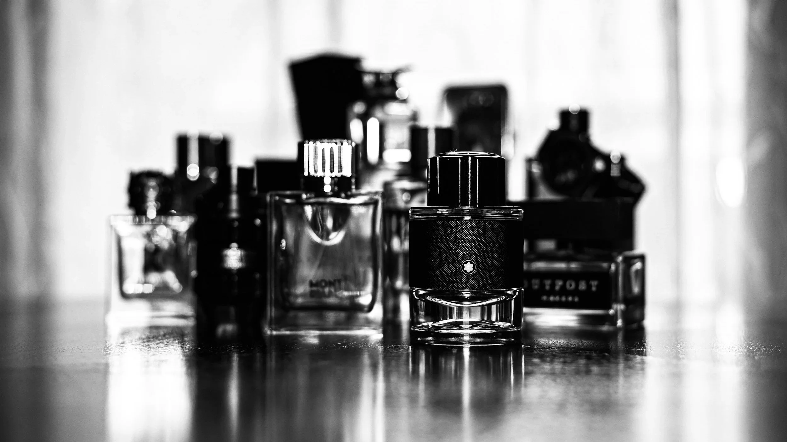 Collection of perfume bottles on a table, black and white photograph.