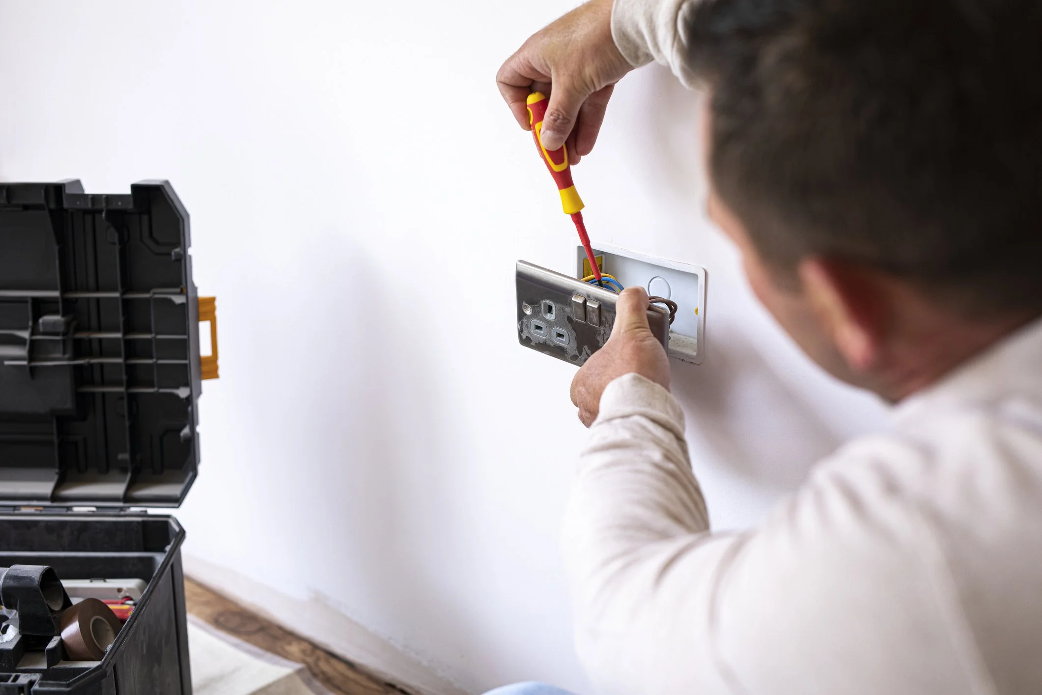 Person installing or repairing electrical outlet with tools, wall open and toolbox nearby.