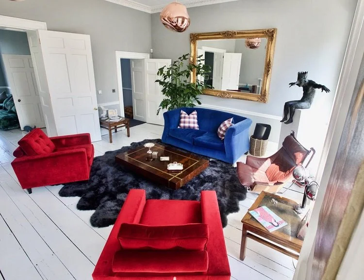 Living room with a blue sofa, red armchairs, a black shag rug, a wooden coffee table, a large mirror, a potted plant, and a decorative horse sculpture.