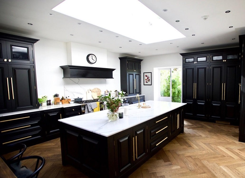 Modern kitchen with black cabinets, white marble island, wood floor, and large skylight.