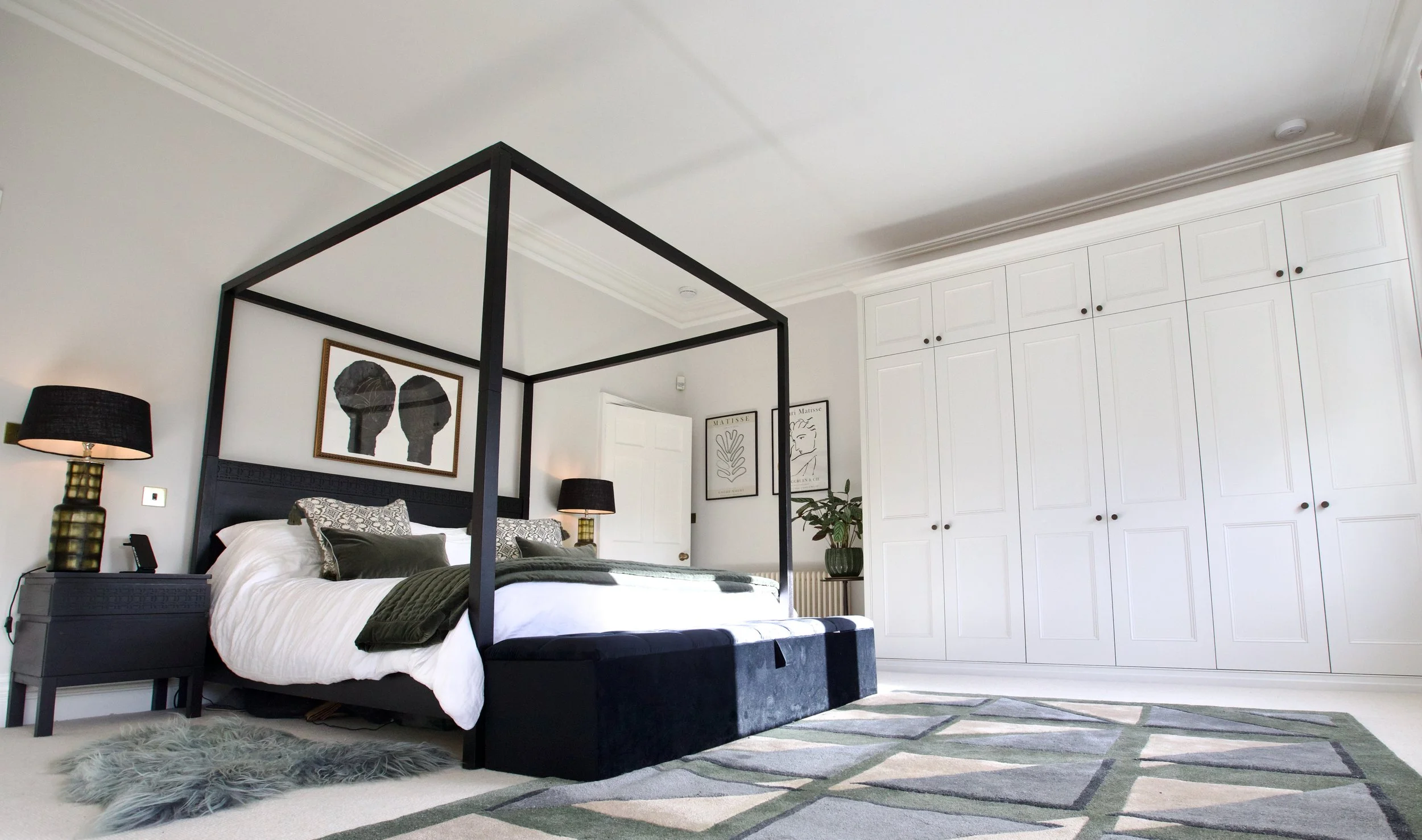 A modern bedroom with a black canopy bed, white bedding, black lamps on nightstands, and white built-in closet doors.
