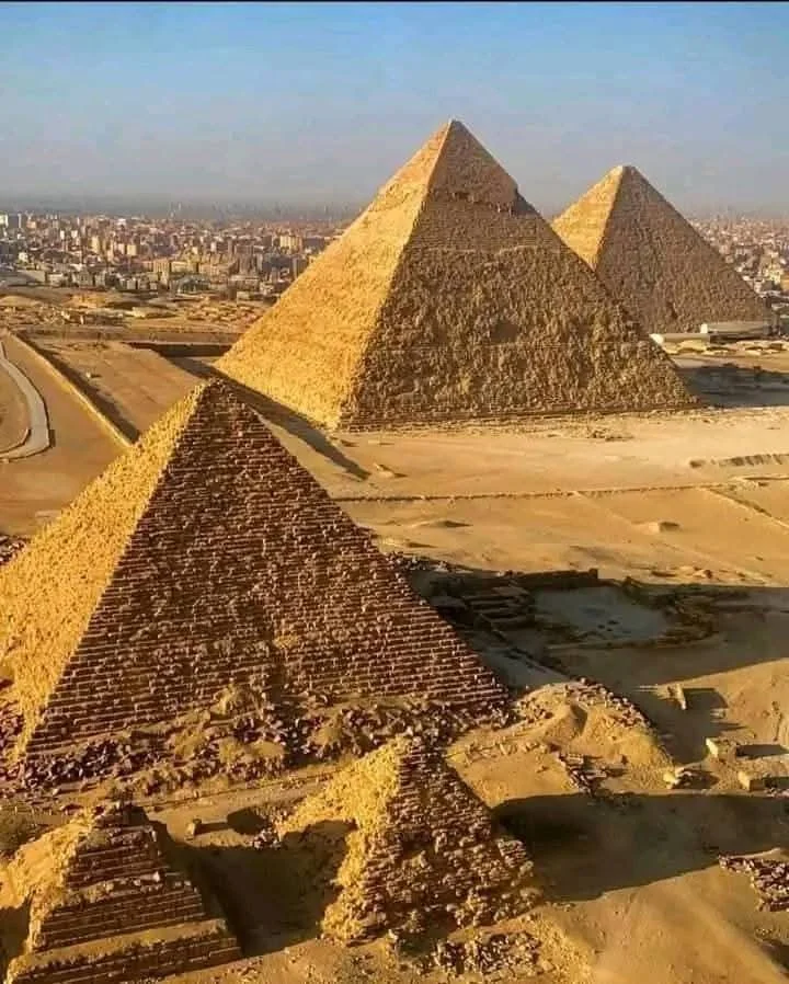 Multiple ancient pyramids in a desert landscape with a modern city in the background.