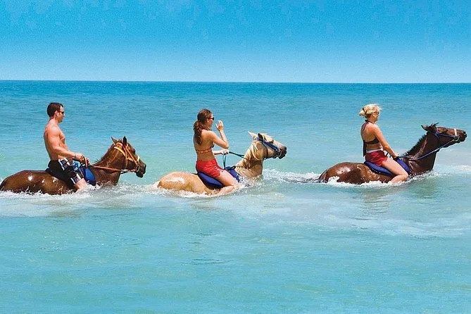 Three people riding horses in the ocean at the beach.
