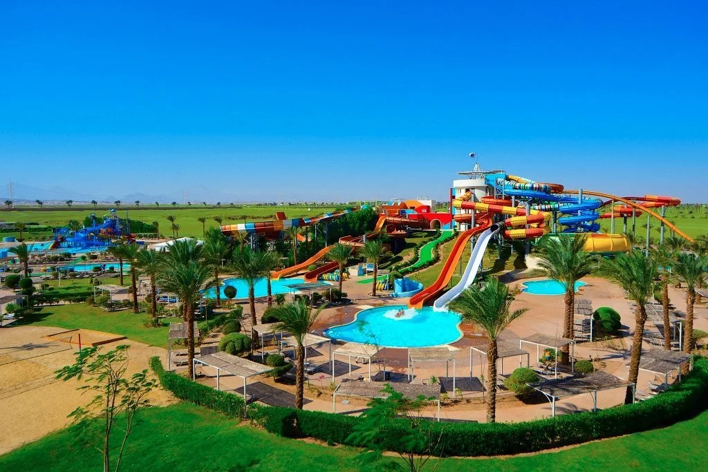 A colorful water park with various water slides, pools, and palm trees set in a sunny outdoor landscape.