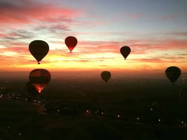 Several hot air balloons floating in the sky during a sunset or sunrise.