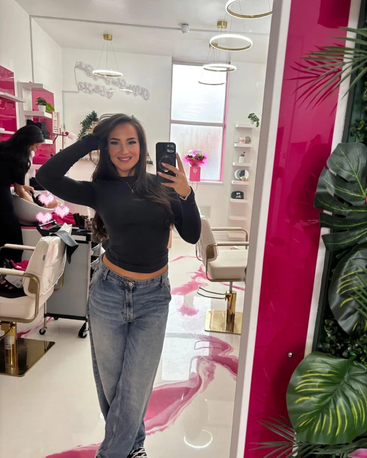 Young woman taking a mirror selfie in a colorful, stylish salon or studio with pink and green decor.