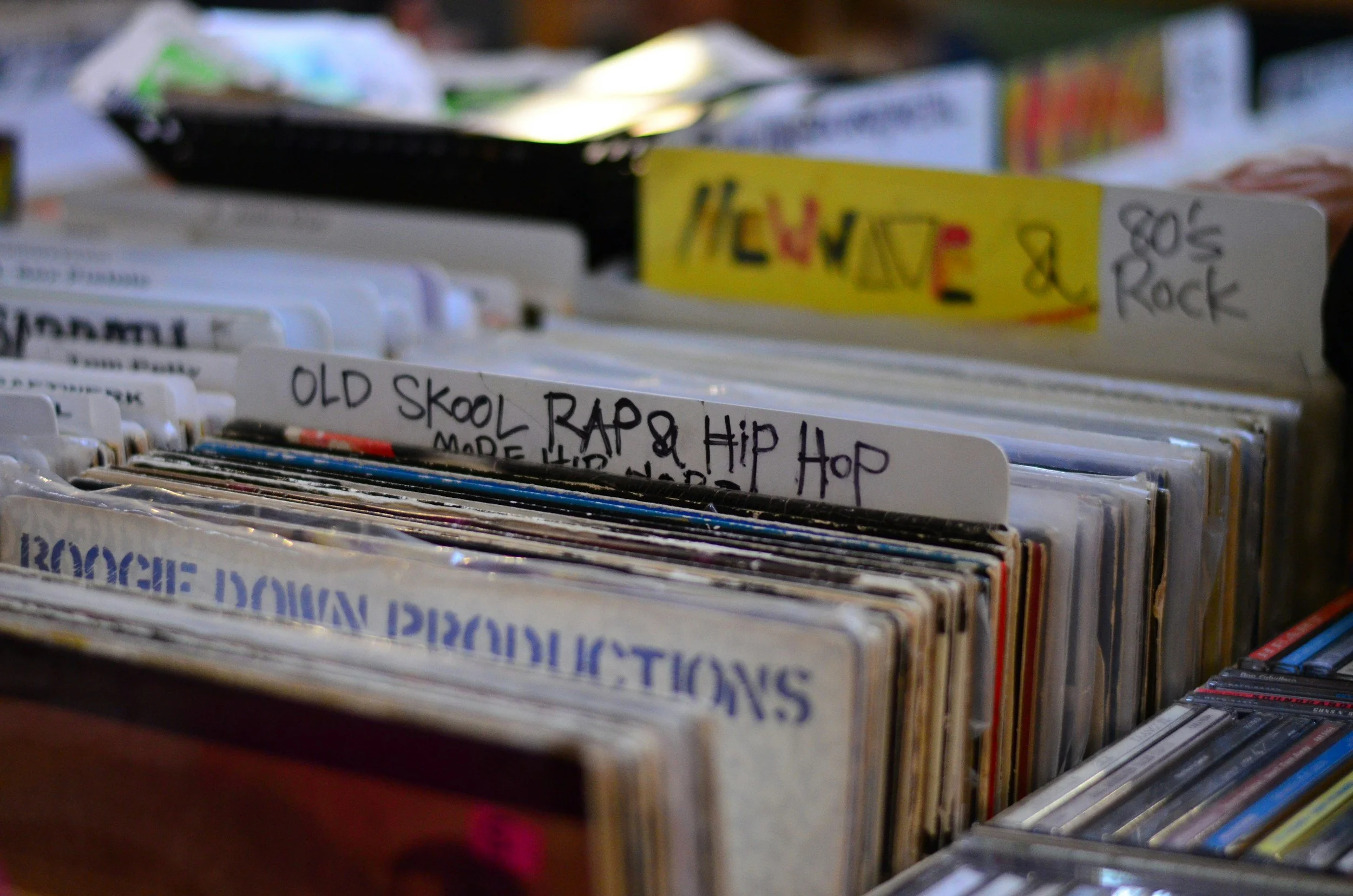 Close-up of vinyl records in a collection, with handwritten labels including 'OLD SKOOL RAP & HIP HOP' and '80'S & ROCK'.