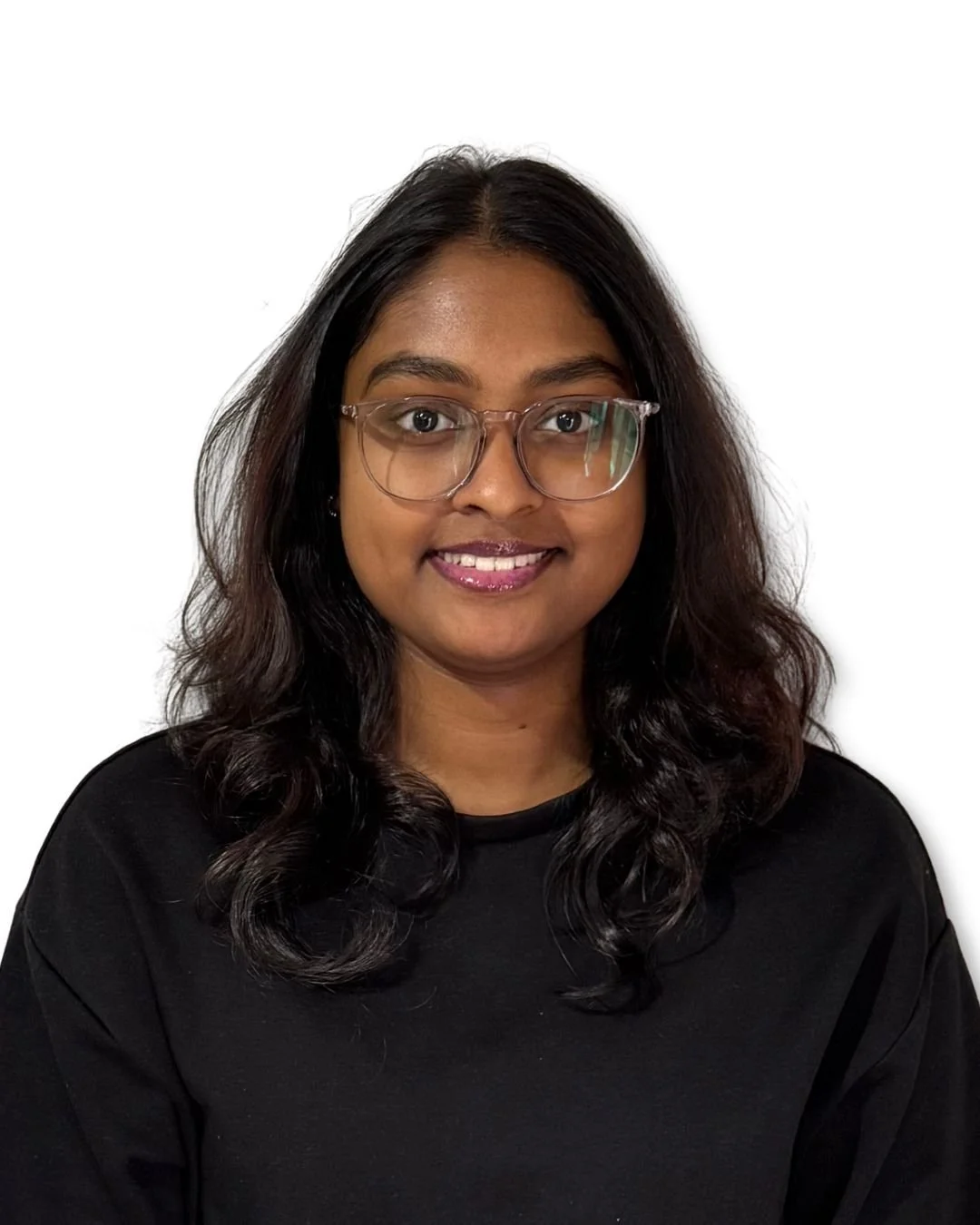 A young woman with shoulder-length wavy black hair, wearing glasses and a black top, smiling against a plain white background.
