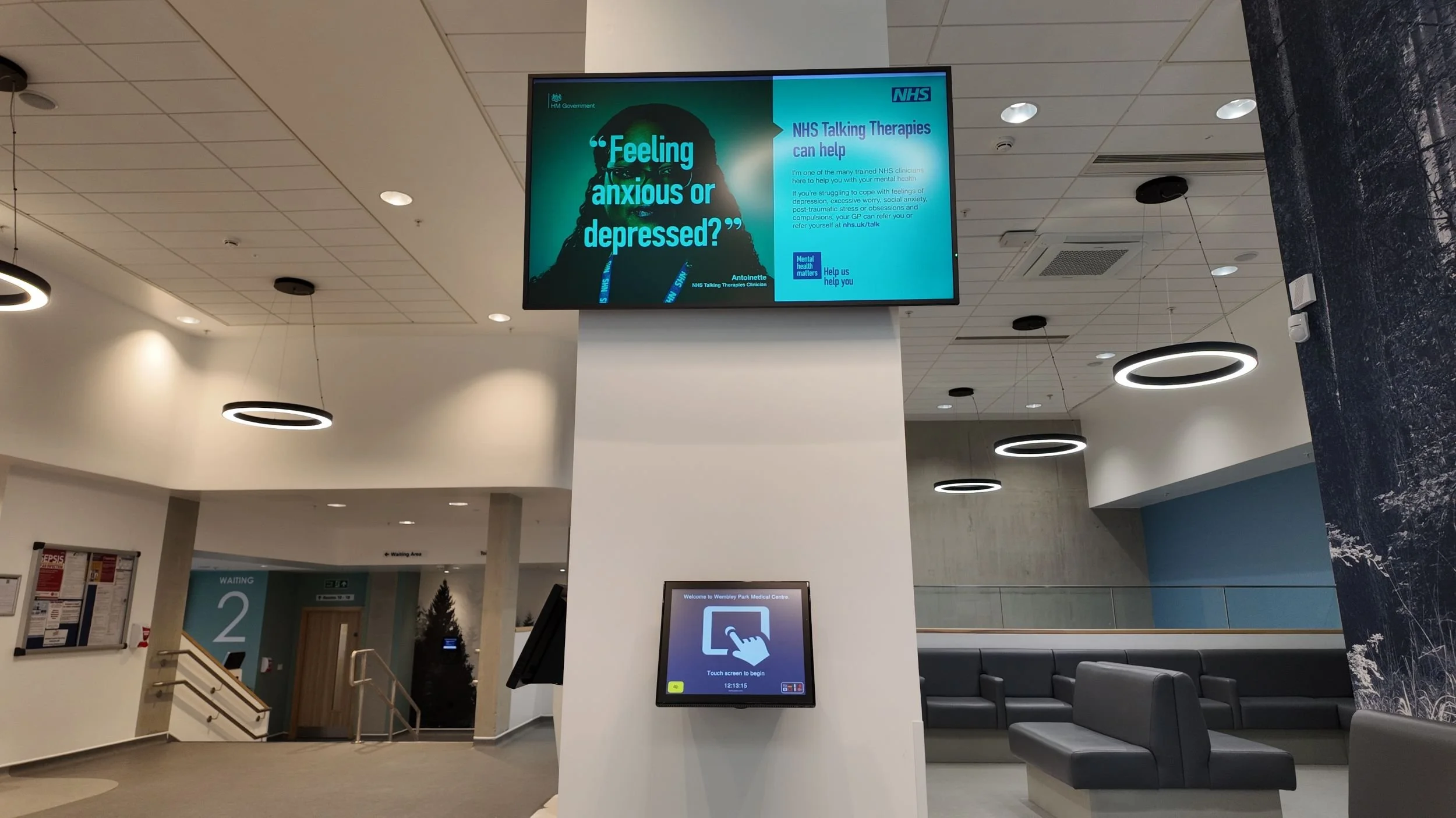 A GP surgery reception area with patient check in touchscreen and patient calling monitor