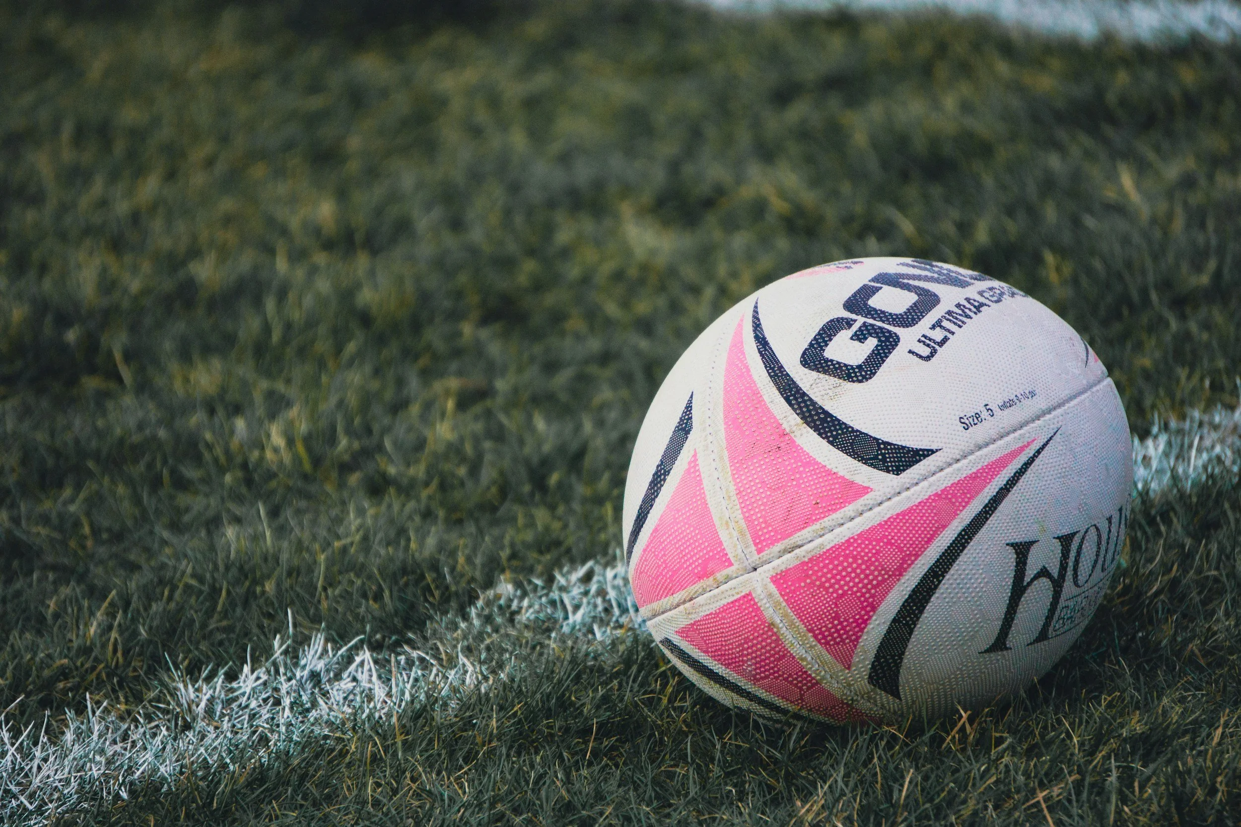 A pink and white rugby ball on a grassy field near a white sideline line.