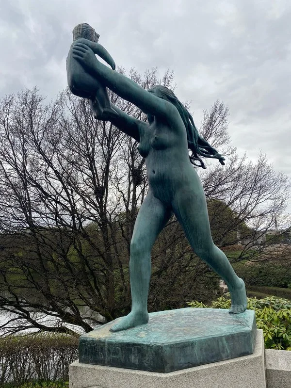 Statua di una donna che solleva un bambino sopra la testa, in un parco con alberi senza foglie in uno sfondo nuvoloso, parco Vigeland a Oslo.