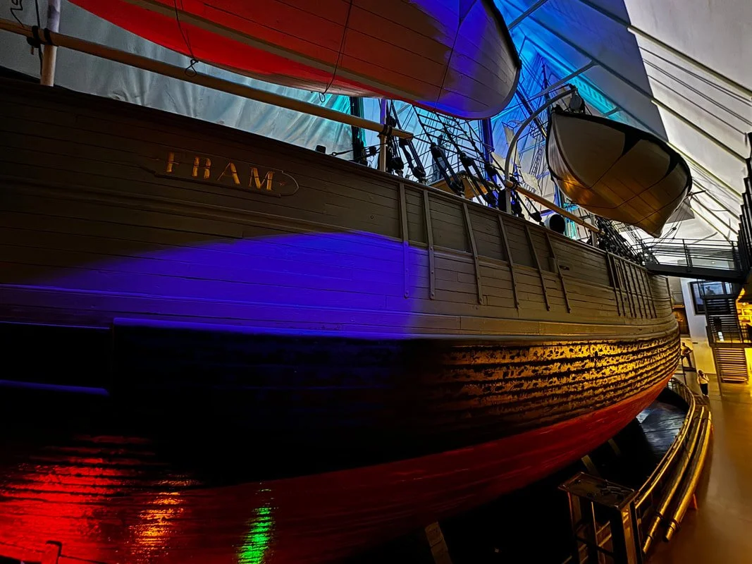 Bambino in un museo che si trova davanti alla nave storica Fram, con luci colorate.