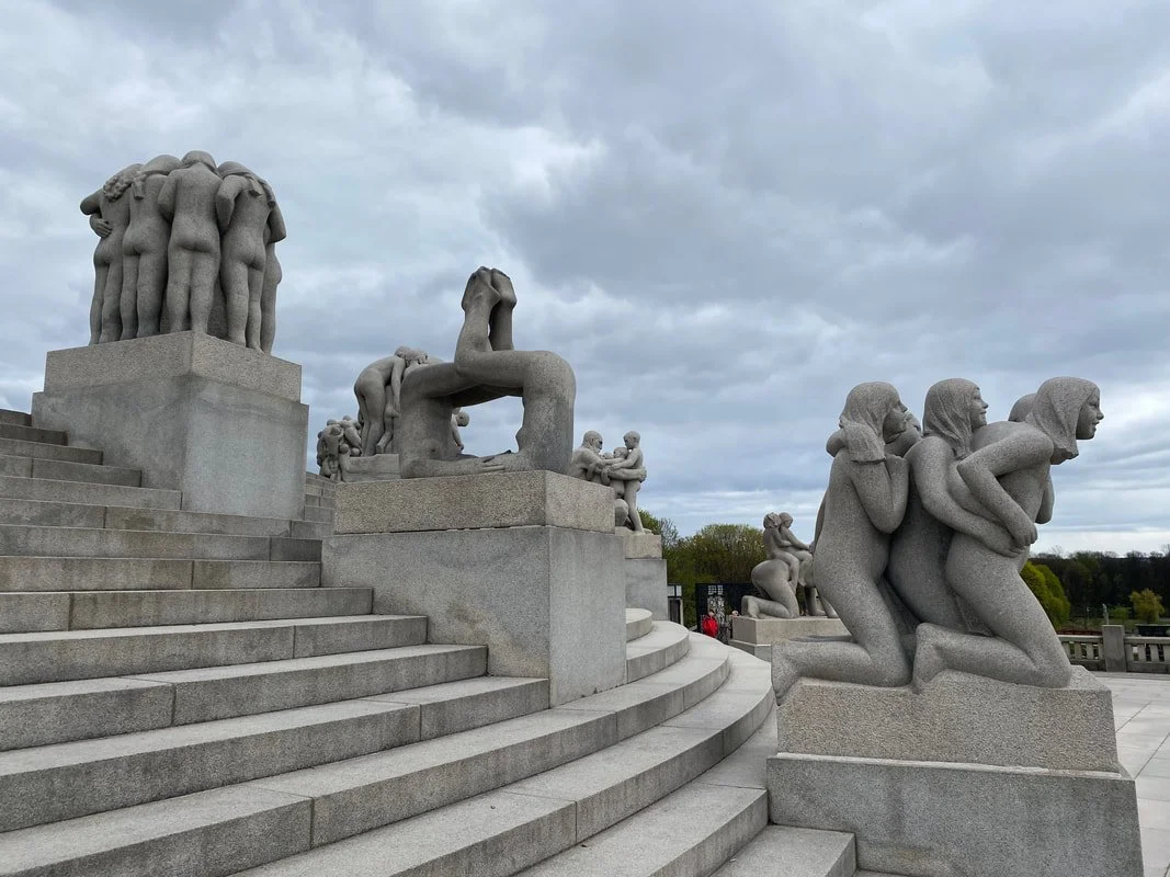 Sculture di pietra che raffigurano gruppi di persone, alcune che si abbracciano e altre che si tengono per mano, collocate su gradini in un'area aperta con cielo nuvoloso, parco Vigeland a Oslo.