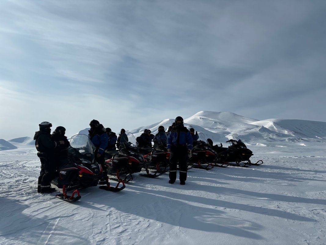 Gruppo di persone con motoslitte in un paesaggio nevoso con montagne e cielo nuvoloso, Tempelfjörd, Isole Svalbard.