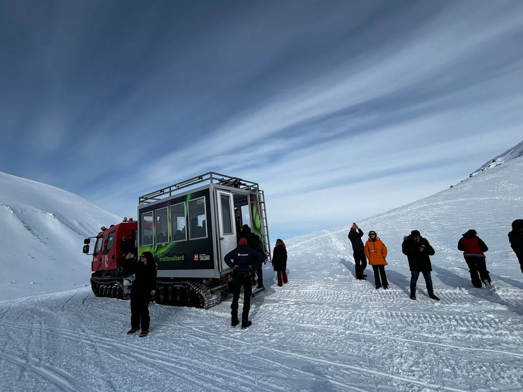 Gruppo di persone in una zona innevata con una motoslitta che trasporta un cabina o un trasportatore per escursionisti di montagna, Isole Svalbard.