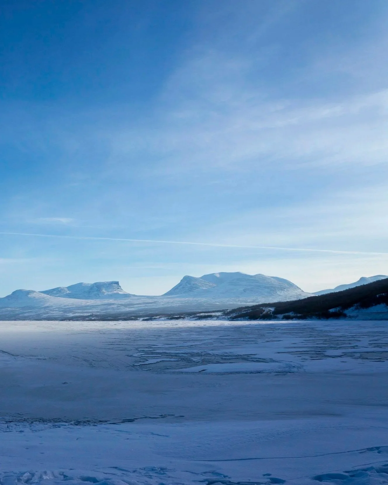 Paesaggio invernale con montagne coperte di neve sotto un cielo azzurro e un campo innevato in primo piano.