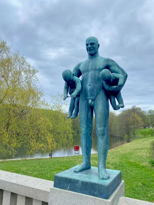 Statua di un uomo nudo che tiene in braccio due bambini, uno su ogni lato, parco Vigeland a Oslo.