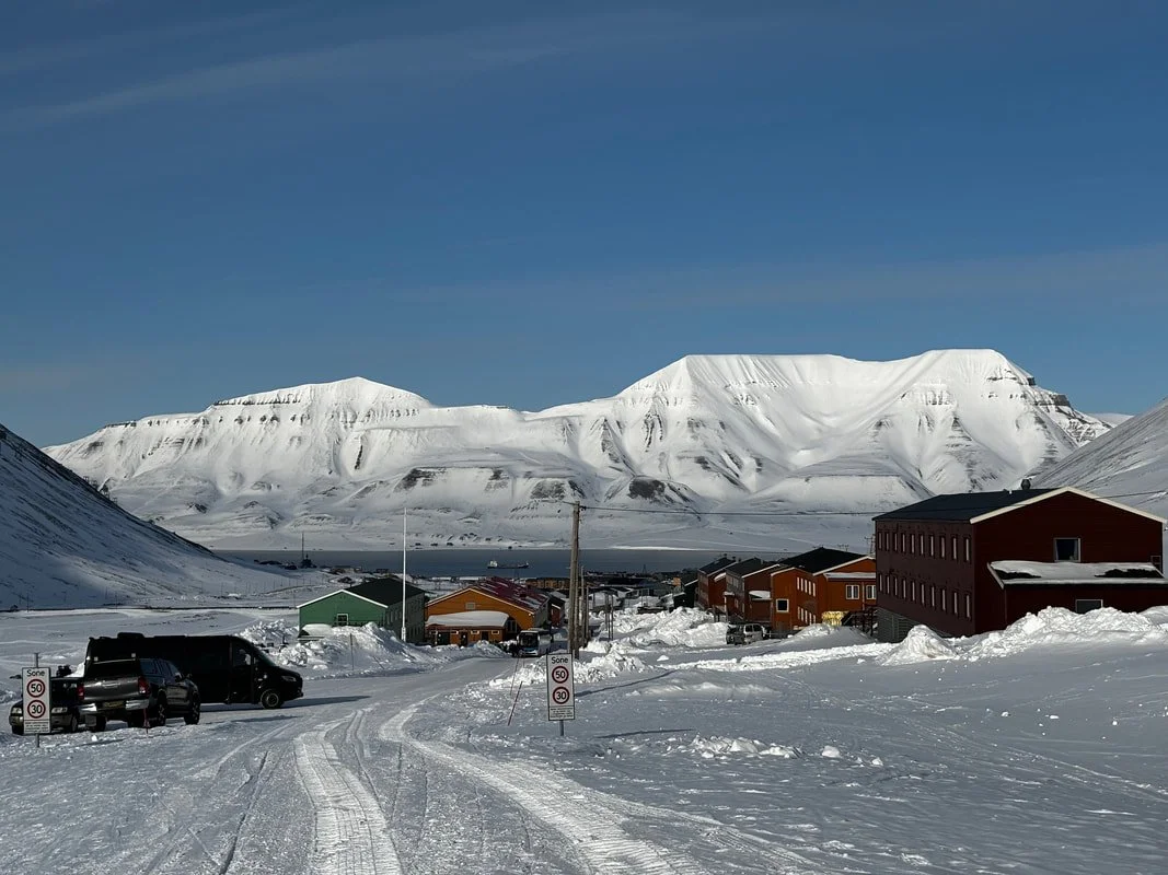 Paesaggio invernale con case colorate in un villaggio tra montagne innevate sotto un cielo blu, Longyearbyen, Isole Svalbard.