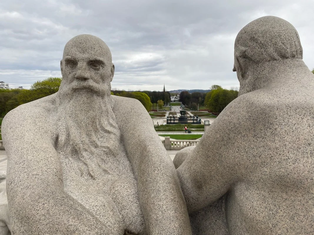 Statue di due uomini seduti uno di fronte all'altro, con un giardino e una fontana sullo sfondo, parco Vigeland a Oslo.