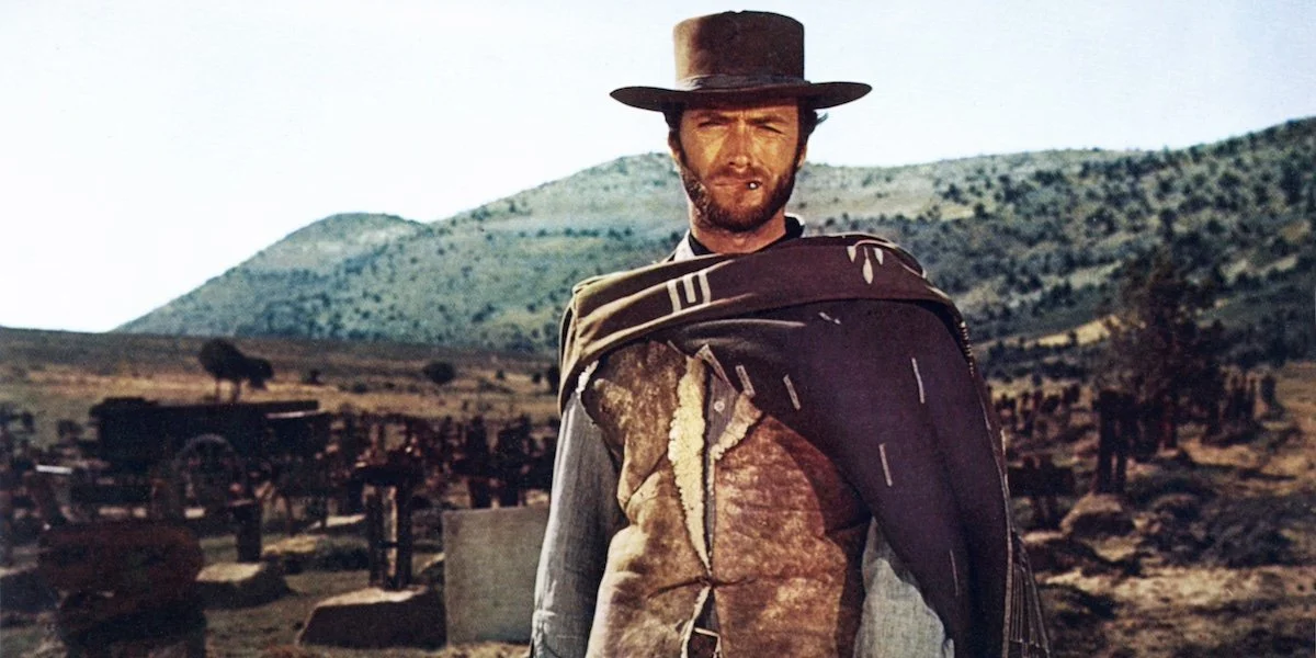 Uomo con cappello grande in un paesaggio arido e montuoso, vestito con abiti vecchi e con un cappotto sopra le spalle, tratto dal film Il buono, il brutto e il cattivo.