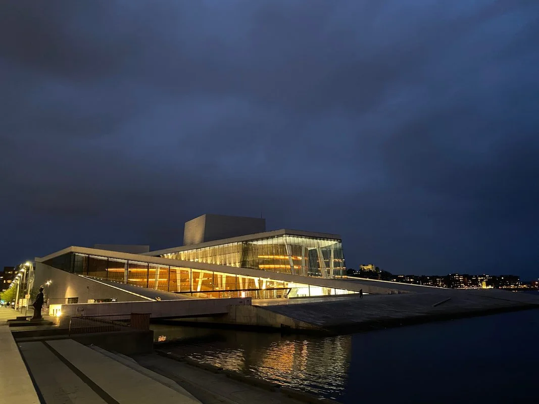 Edificio moderno illuminato di notte con luci calde, situato vicino all'acqua, sotto un cielo scuro a Oslo.